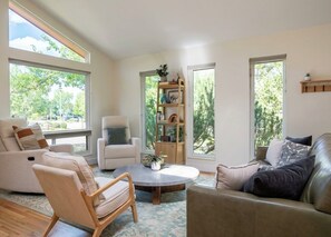 A spacious living room with a round coffee table, two sofas, a bookshelf, and large windows offering a view of trees. - Spacious Boulder Home Perfect for Sundance - Near CU, Downtown, & Boulder Trails (Boulder)
