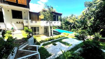 Une maison moderne à deux étages, dotée d’une piscine, entourée d’une végétation luxuriante et d’un jardin bien entretenu.