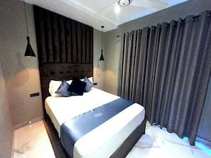Un dormitorio moderno con una cama grande, dos lámparas colgantes, un cabecero y un ventanal con cortinas.