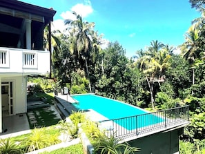 Una piscina rodeada de exuberante vegetación y un edificio de dos pisos con balcón.