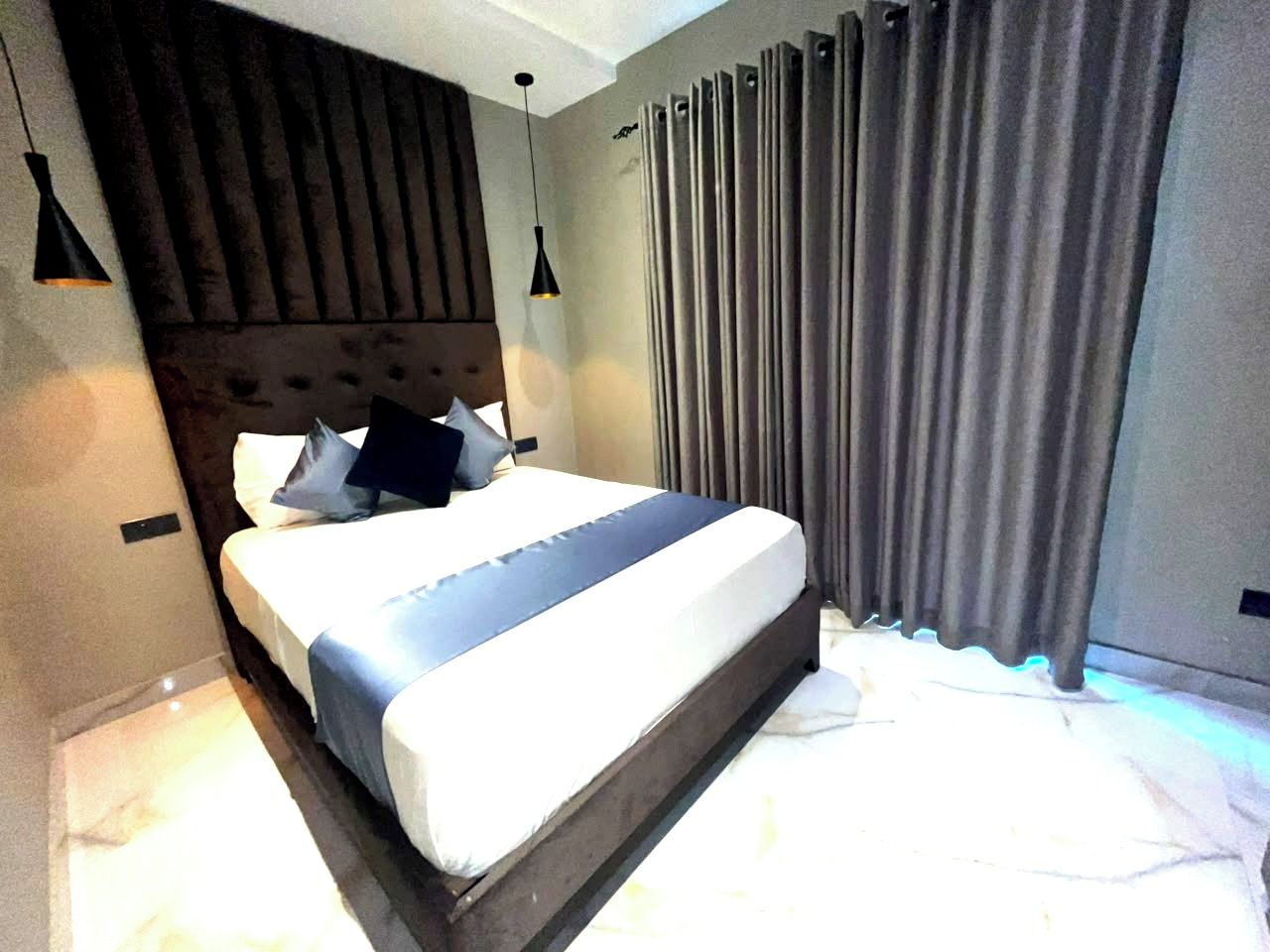 Un dormitorio moderno con una cama grande, cabecera y cortinas.