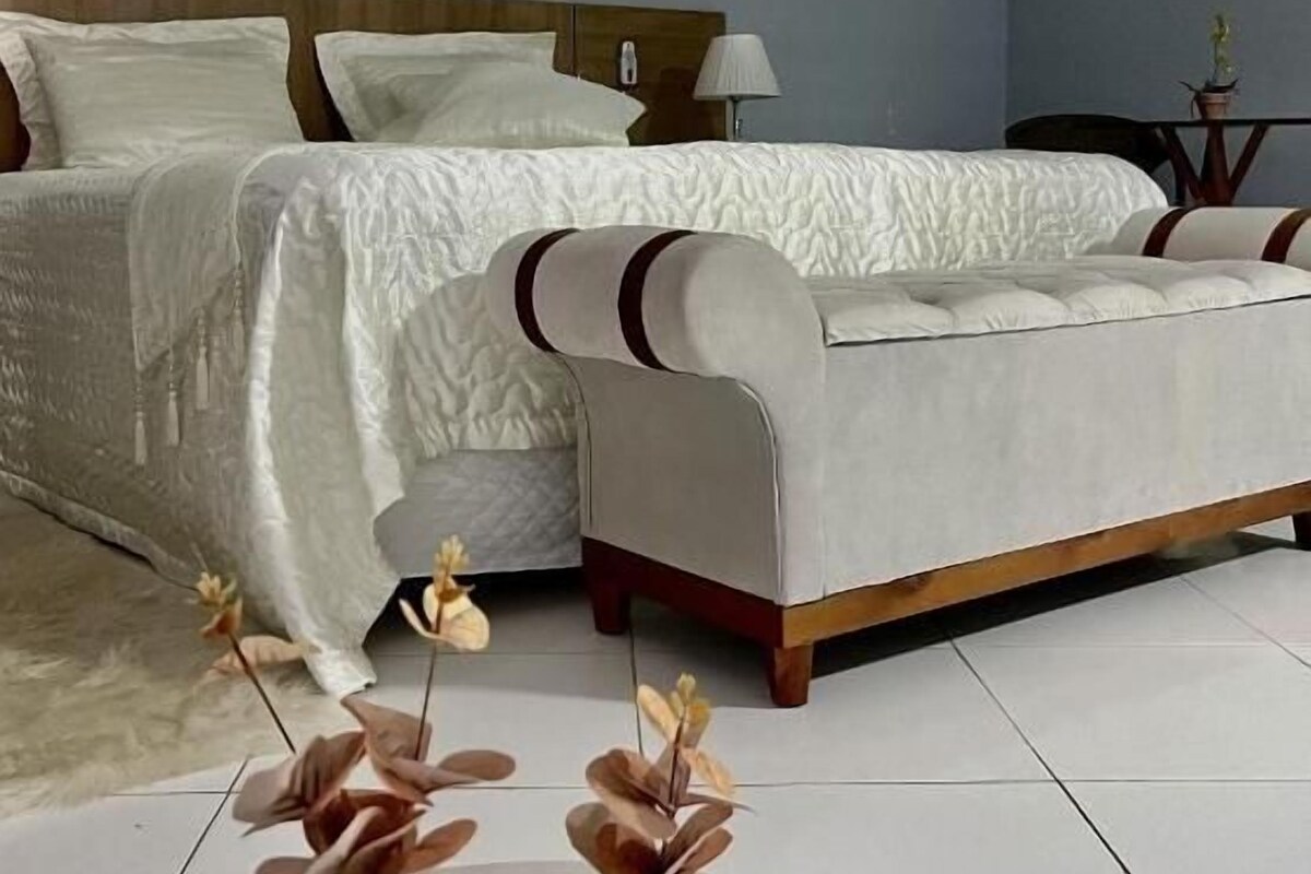 A bedroom with a bed, a sofa, a painting on the wall, and two vases on the floor.