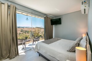 A bedroom with a bed, a TV, a balcony with a chair, and a view of the countryside. - Hotel Extrema Club (Extrema)