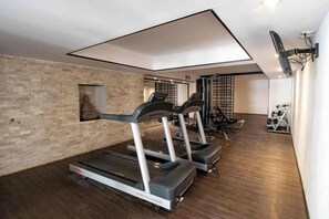 Een fitnessruimte met loopbanden, een tv aan de muur en een houten vloer.
