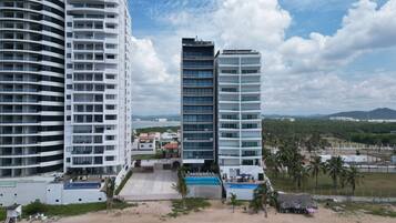 A high-rise hotel with multiple balconies, a swimming pool, and a view of the surrounding landscape.
