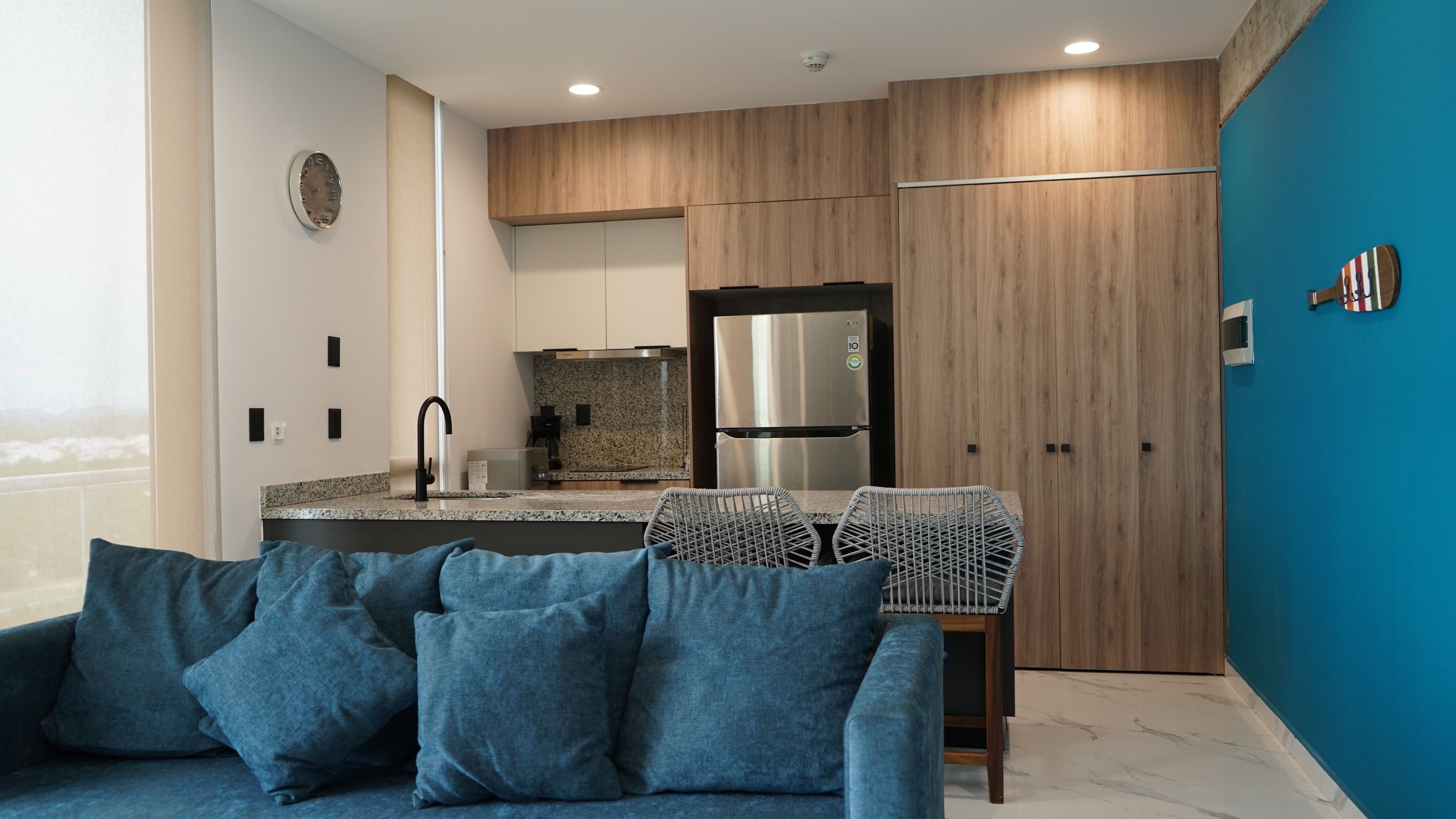 A modern kitchen with a built-in oven, a stainless steel refrigerator, and a dining area with a metal chair.