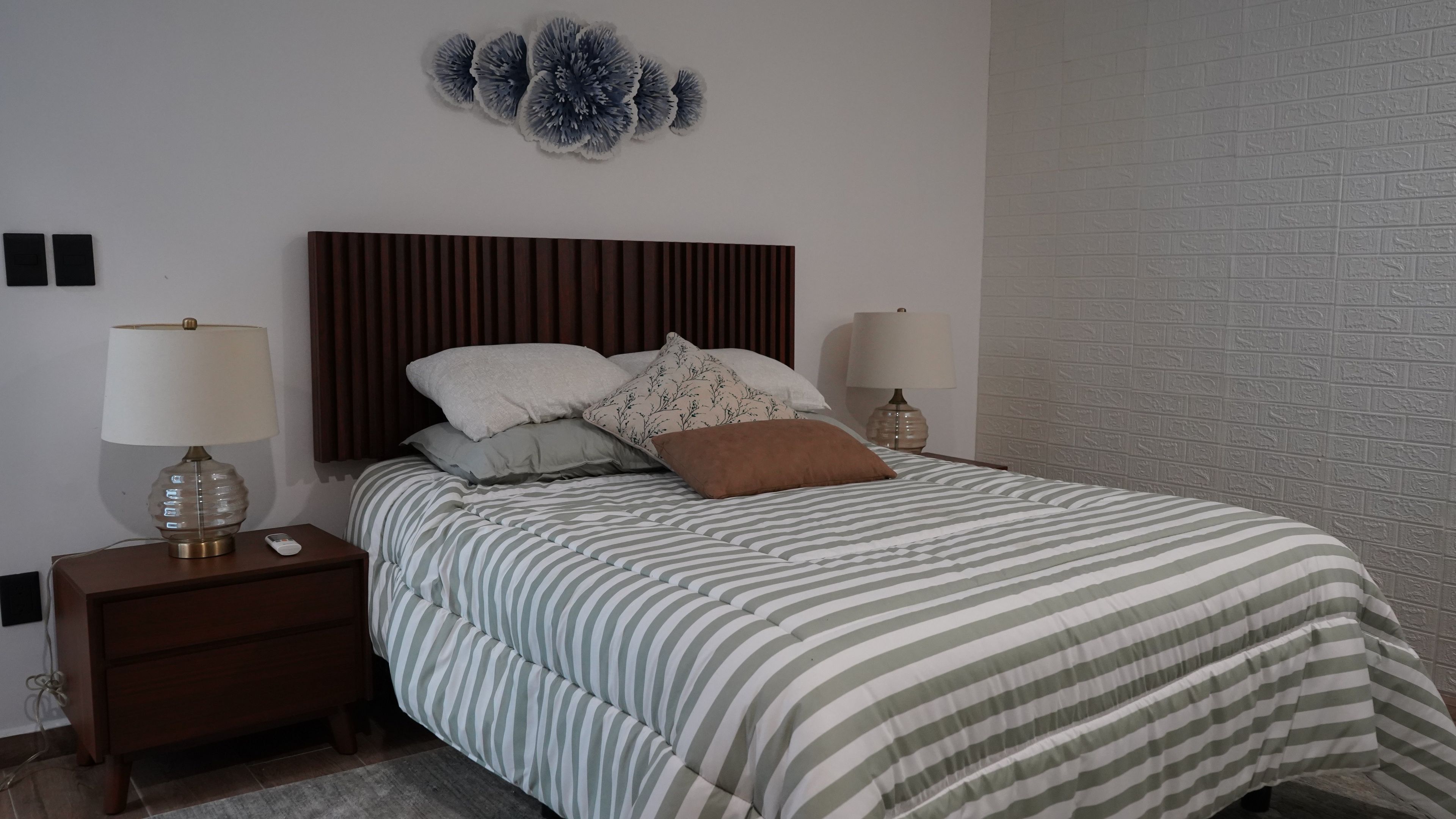 A bedroom with a striped bedspread, a wooden headboard, two bedside lamps, and a decorative wall piece.