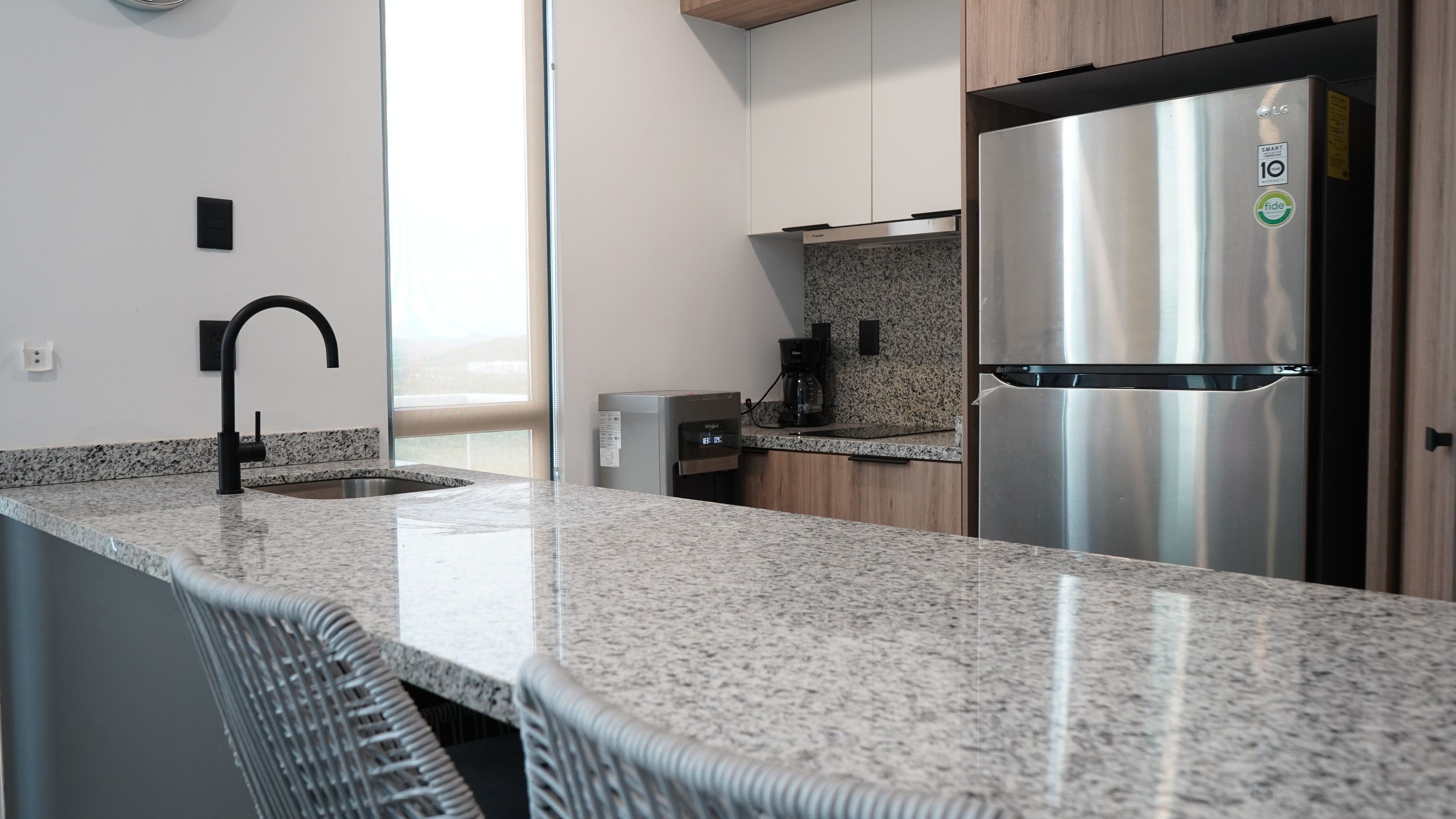 A modern kitchen with granite countertops, a stainless steel refrigerator, a built-in oven, and a coffee maker.