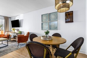 A modern living room with a round dining table, wicker chairs, a flat-screen TV, and decorative wall art. - Sunset Harbor Palms 1-204 (Navarre)