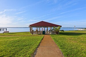 A gazebo with a red roof overlooking a lake, a walking path leading to it, and a bench to the left. - Sunset Harbor Palms 1-204 (Navarre)