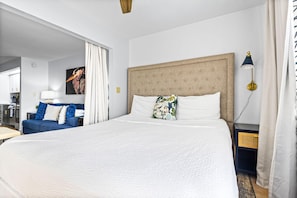 A hotel room with a large bed, a sofa, a nightstand, a lamp, and a painting on the wall. - Sunset Harbor Palms 1-204 (Navarre)