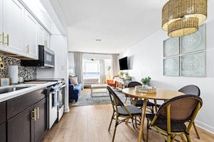 Una cocina moderna con comedor, que cuenta con un amplio ventanal, una mesa de comedor con sillas y un televisor montado en la pared.