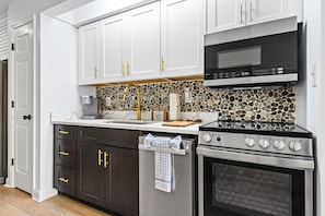 A kitchen with white cabinets, a black microwave, a stainless steel oven, and a stone backsplash. - Sunset Harbor Palms 1-204 (Navarre)