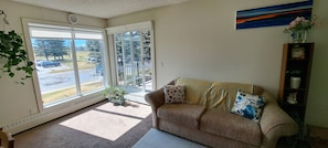 A living room with a sofa, a window, a radiator, and a painting on the wall. - Luxury & homely Apartment. Close to Calgary airport, bus stop and shopping mall. (Airdrie)