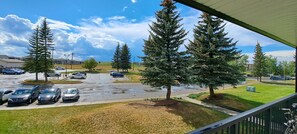 A parking lot with several cars, trees, and a building in the background. - Luxury & homely Apartment. Close to Calgary airport, bus stop and shopping mall. (Airdrie)