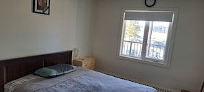 A bedroom with a bed, a window, a clock, and a small table with a vase. - Luxury & homely Apartment. Close to Calgary airport, bus stop and shopping mall. (Airdrie)