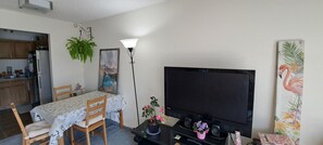 A living room with a dining table, chairs, a TV, a lamp, and a painting.