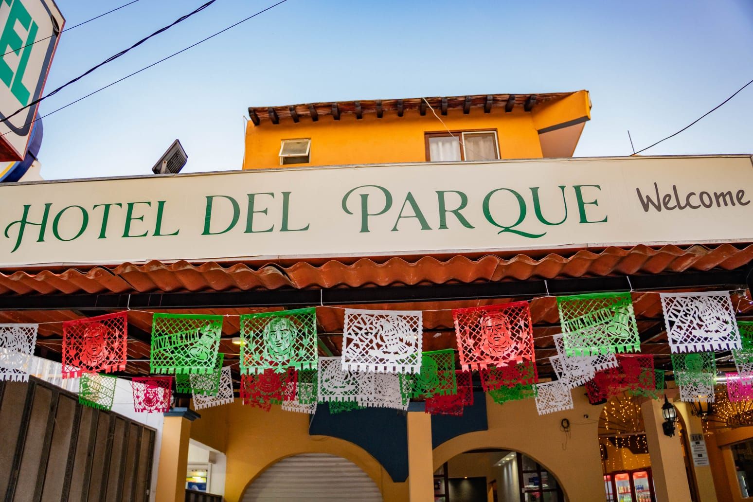 Un hotel llamado 'Hotel Del Parque' con un letrero de bienvenida y coloridos adornos de papel.