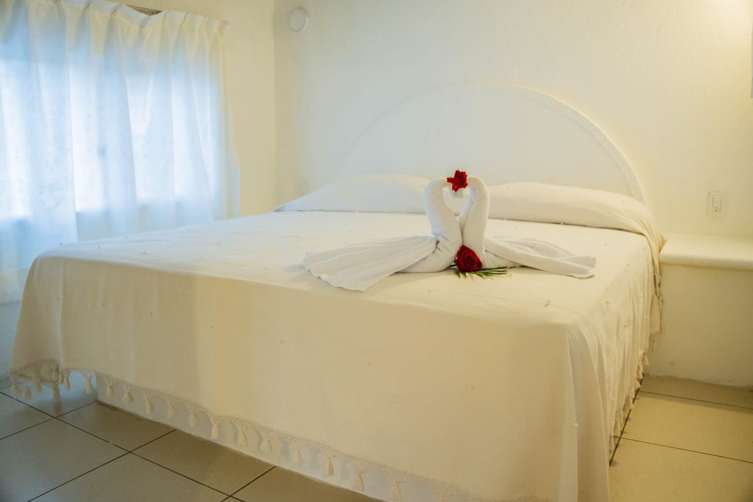 Una habitación de hotel con una cama bien hecha, una rosa roja y una decoración con forma de cisne blanco.