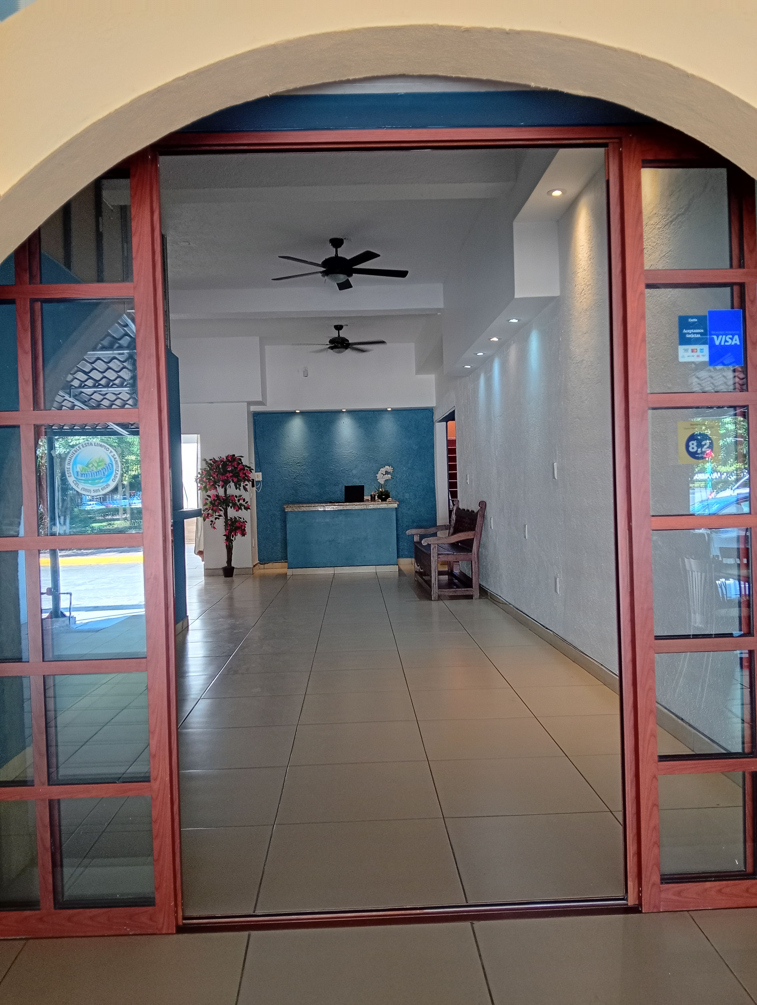 Vestíbulo de hotel con mostrador de recepción, zona de estar, ventiladores de techo y vistas al exterior.