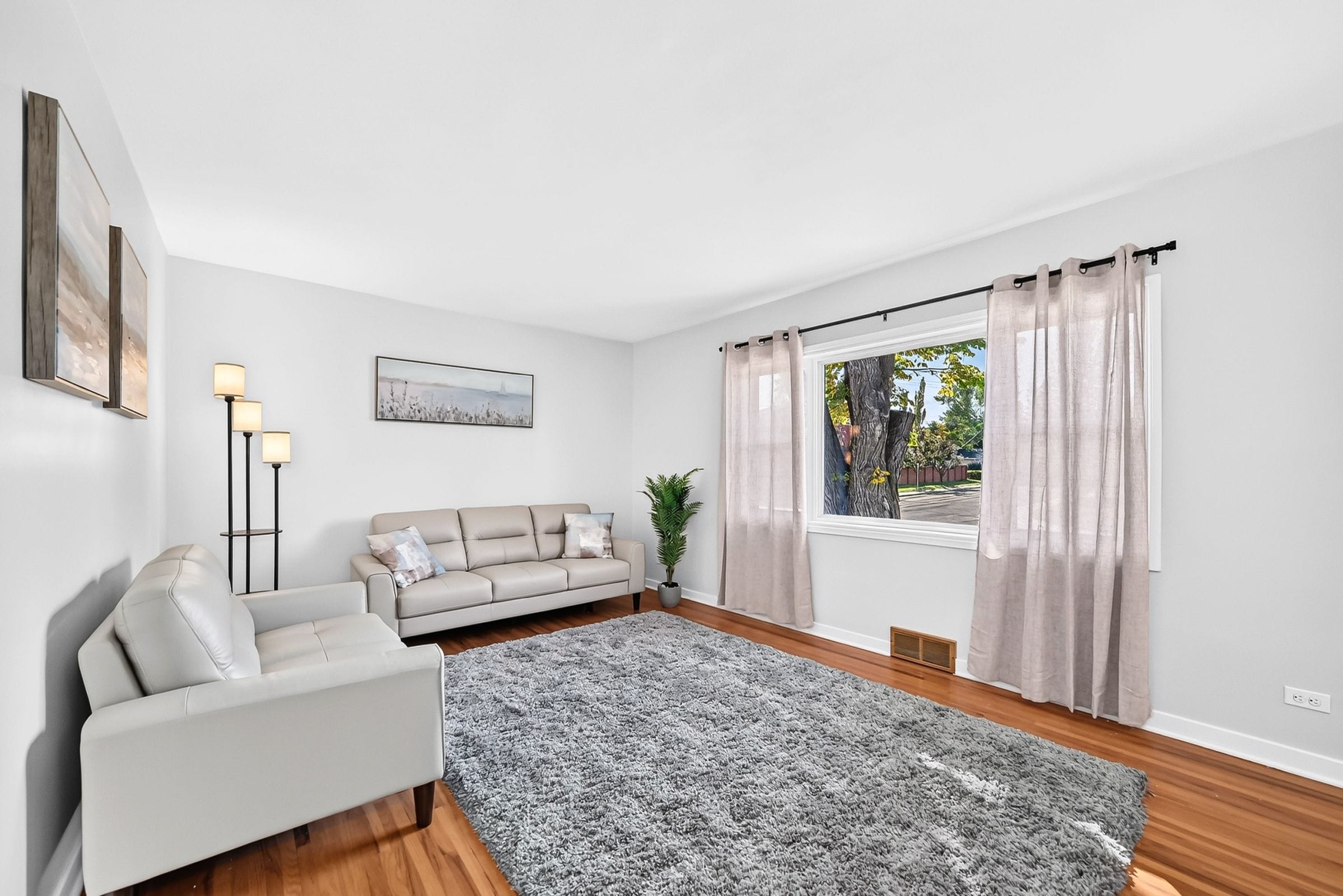 A modern living room with a sofa, a rug, a floor lamp, and a window with curtains.