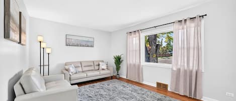 A modern living room with a sofa, a rug, a floor lamp, and a window with curtains.
