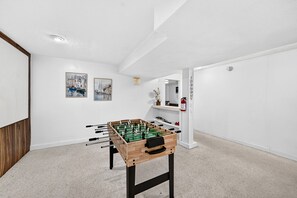 Une pièce avec une table de baby-foot, des murs blancs et deux tableaux encadrés.