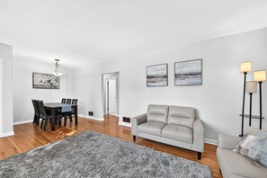 Un salon moderne avec un canapé gris, une table à manger avec des chaises et deux œuvres d’art encadrées accrochées au mur.