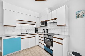 Une cuisine de taille réduite avec des meubles blancs, un lave-vaisselle, une cuisinière et un four à micro-ondes.