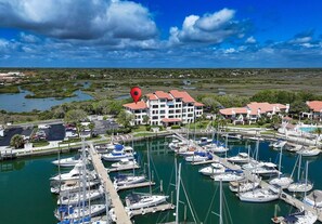 A marina with multiple boats docked, a large building with a red roof, and a body of water with greenery in the background. - Waterfront Luxury 2 BR Ground Floor St. Augustine FL (St. Augustine)