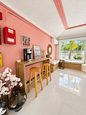 A modern kitchen with a pink wall, wooden bar counter, two stools, and a coffee machine. - #14 – Cozy & Functional Studio w/Queen Bed, Work Desk, Kitchen and Free Parking (Miami)