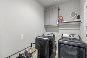 Une buanderie équipée de deux machines à laver à chargement frontal, d’une étagère contenant de la lessive et d’un porte-linge.