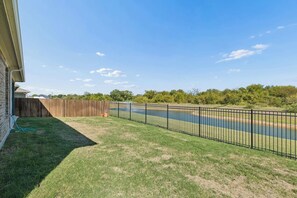 Un jardin avec une clôture en bois, une clôture en métal et une étendue d’eau.