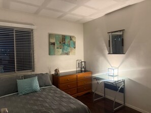 Un dormitorio con cama, cómoda, escritorio y una obra de arte en la pared.