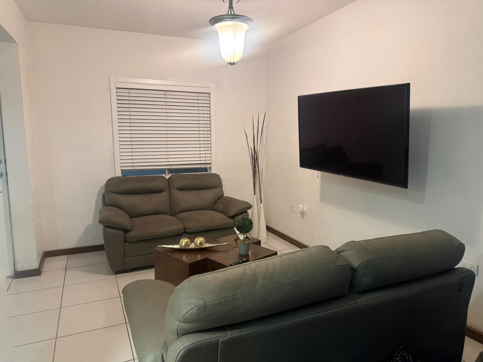 A living room with a flat-screen TV mounted on the wall, a brown sofa, a grey sofa, and a coffee table with decorative items.