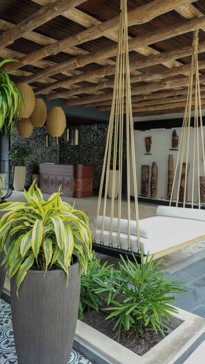 Un espace de détente moderne avec un fauteuil suspendu, une grande plante en pot et un mur décoré de motifs.