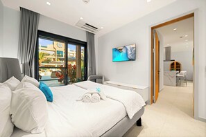 Une chambre d’hôtel comprenant un lit, un bureau, une chaise, une vue sur une piscine et des bâtiments, ainsi qu’une porte donnant accès à une salle de bain.