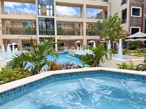 A hotel pool area with multiple levels, water fountains, and palm trees. - Walk-Out to Pool |Jacuzzi, BBQ & White Sand Lounge (Noord)
