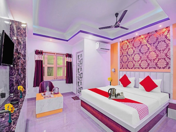 A hotel room with a bed, a desk, a window with curtains, an air conditioning unit, and a ceiling fan.