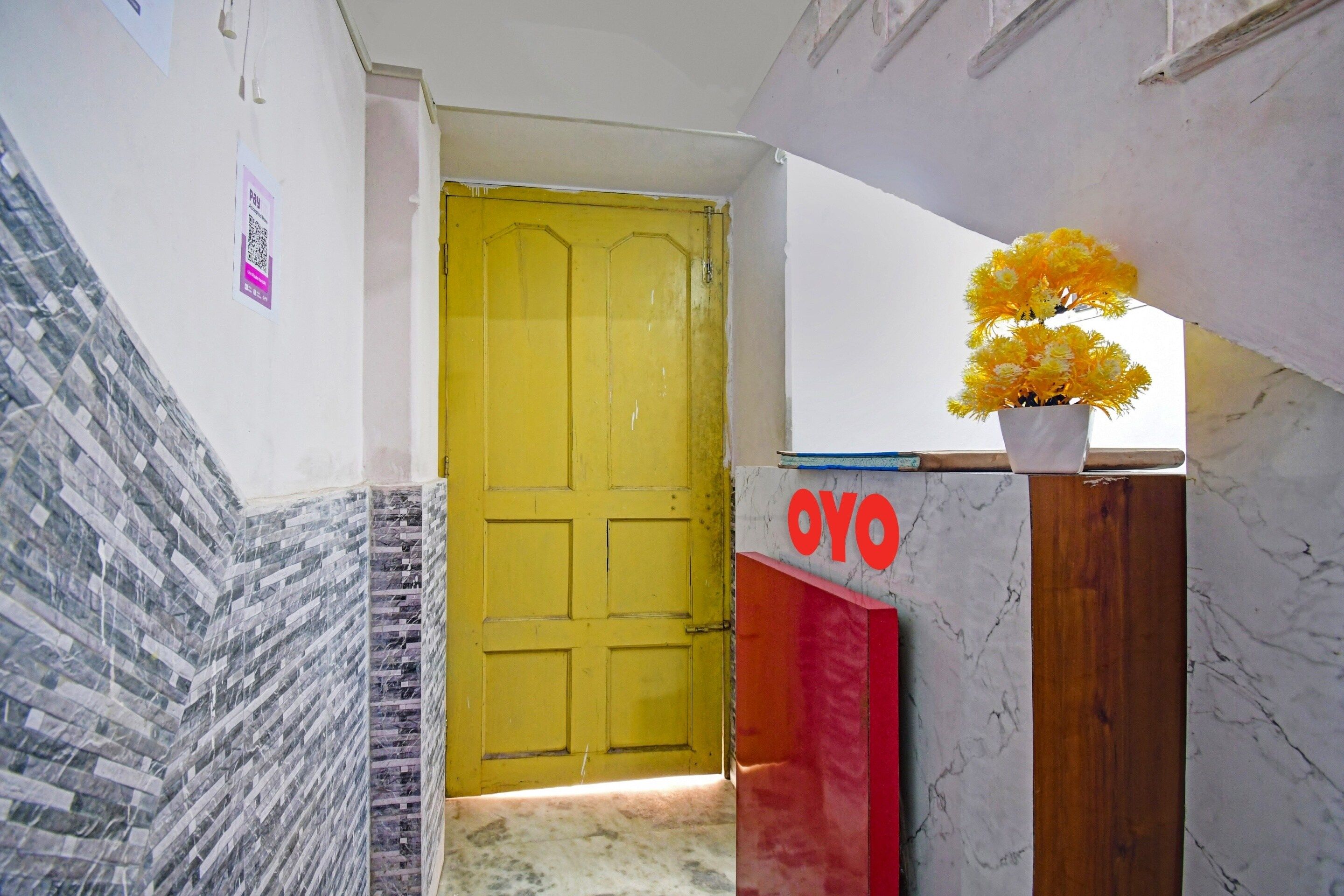 Una puerta amarilla con un letrero que dice 'OYO' y una maceta con flores amarillas.