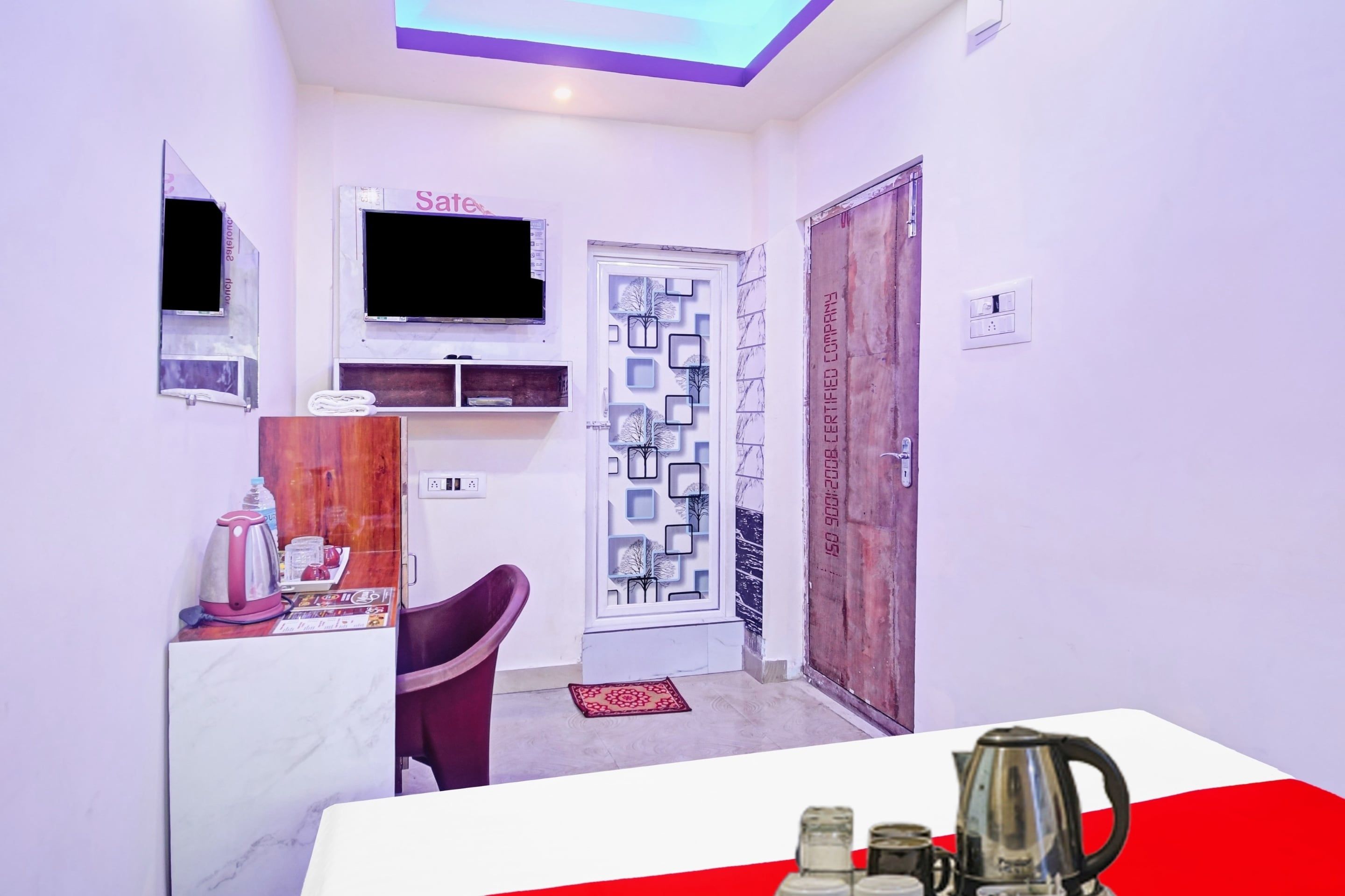 Una habitación pequeña con televisión, una mesita con tetera, una silla y una puerta con diseño decorativo.