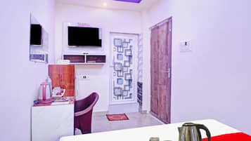 Una habitación pequeña con televisión, una mesita con tetera, una silla y una puerta con diseño decorativo.