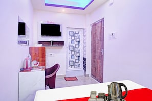 Una habitación pequeña con televisión, una mesita con tetera, una silla y una puerta con diseño decorativo.