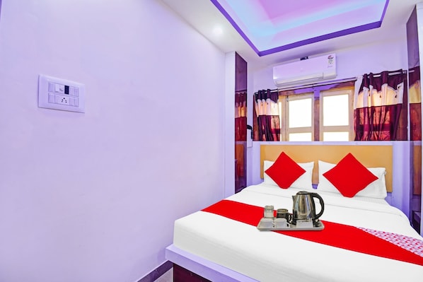 Una habitación de hotel con una cama, una ventana con cortinas, un equipo de aire acondicionado y un enchufe en la pared.