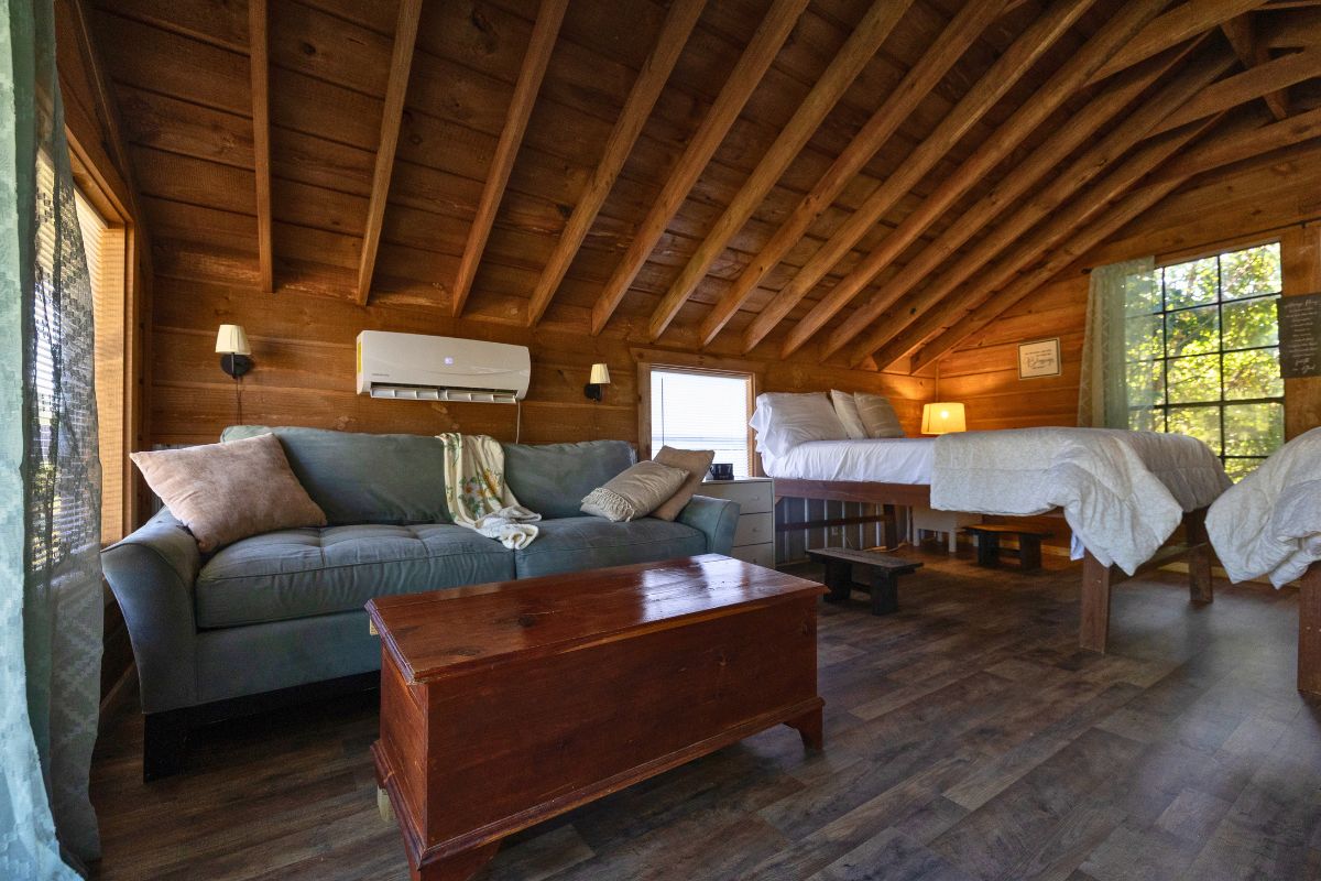 Un chalet confortable avec un plafond en bois, un canapé, une table basse en bois et un lit recouvert d’une courtepointe blanche.