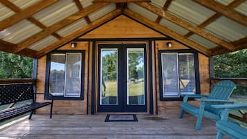 A covered porch with a wooden roof, a bench, and two Adirondack chairs.
