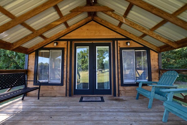 A covered porch with a wooden roof, a bench, and two Adirondack chairs.