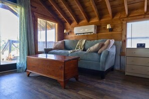 Una stanza accogliente con soffitto in legno, un divano, un settimino in legno e un condizionatore d'aria.