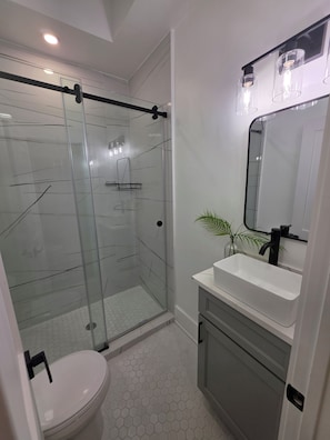 Ein modernes Badezimmer mit einer gläsernen Duschkabine, einem weißen Waschbecken mit schwarzem Wasserhahn und einem Spiegel über dem Waschbecken.