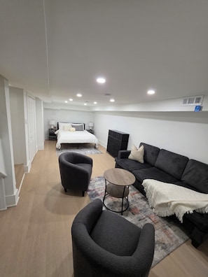 Ein modernes Hotelzimmer mit einem Bett, zwei Sesseln, einer Couch, einem kleinen Tisch und einem gemusterten Teppich.